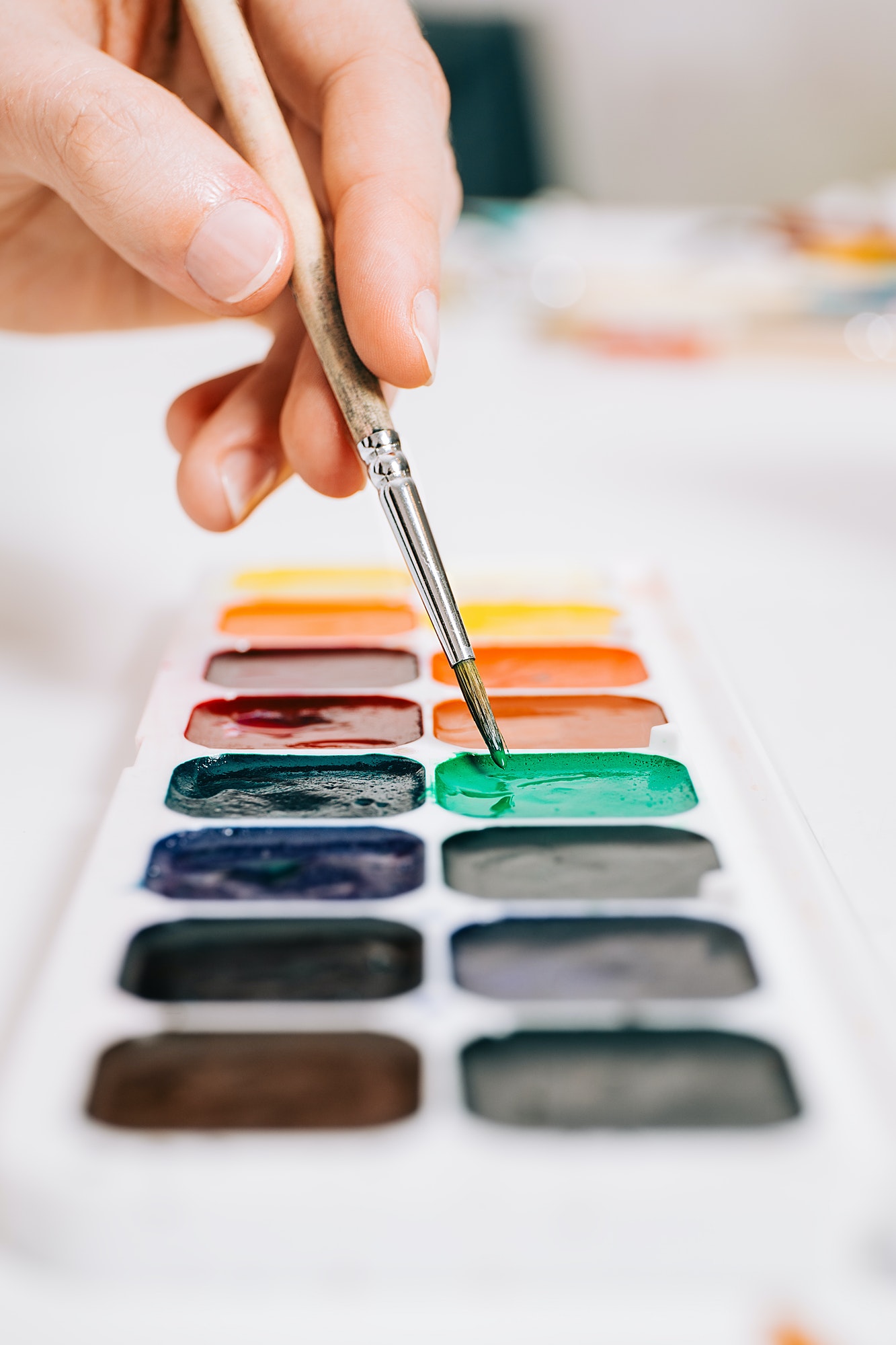 Close up view of hand holding a brush and mixing the colors of paints on palette.